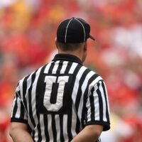A football umpire in uniform overseeing the game in a crowded stadium.