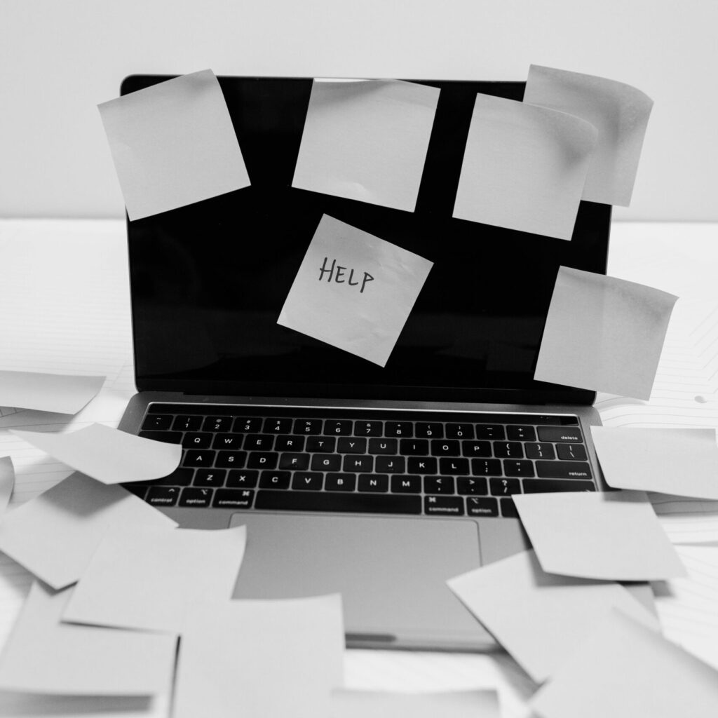 Black and white photo of a laptop covered with sticky notes, one labeled 'HELP'.
